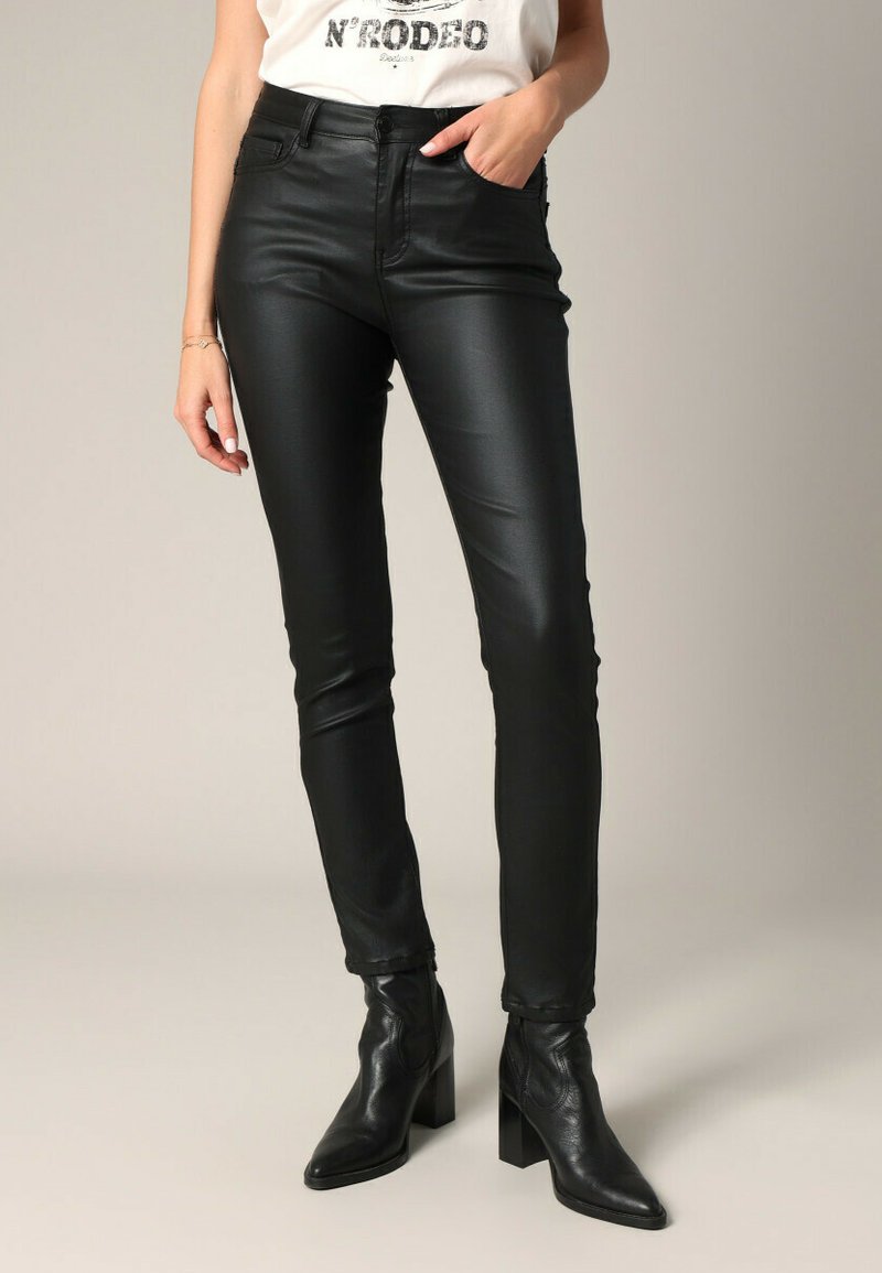 Zwarte faux leren skinny broek met een gladde textuur en vijf-pocket ontwerp, gecombineerd met zwarte hoge enkelschoenen.