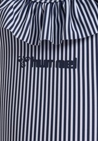 Marinblått och vitt randigt tyg med en volang på halsringningen. Har en framträdande "hummel"-logotyp i matchande marinblå färg.