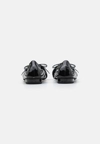 Chaussures en cuir verni noir avec un bout rond, un petit talon et des lacets décoratifs. La vue arrière met en valeur la texture lisse et brillante ainsi que les lignes épurées.