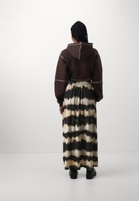 Korte bruine hoodie met lichte stiksels, gecombineerd met een lange rok met een golvend zwart, bruin en crèmekleurig tie-dye patroon. Zwarte laarzen.
