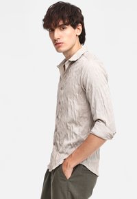 Camicia button-up grigio chiaro, con trama e un motivo sottile, maniche lunghe arrotolate e design del colletto rilassato.