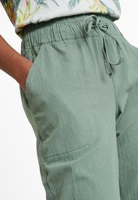 Pantalon vert clair texturé avec une taille élastique et un cordon de serrage. Dispose de poches latérales et d'une coupe ample.