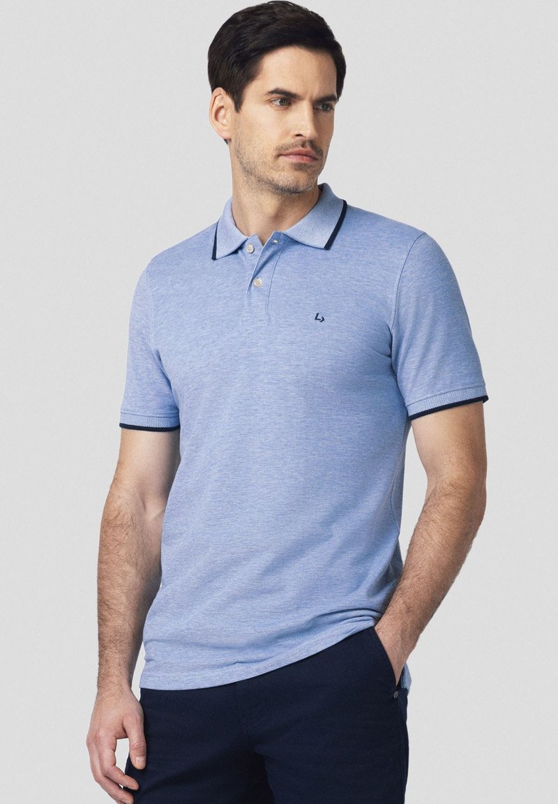 Jasnoniebieska koszulka polo wykonana z miękkiego materiału, z klasycznym kołnierzykiem, posiadająca granatowe akcenty na kołnierzyku i rękawach oraz małe logo na klatce piersiowej.