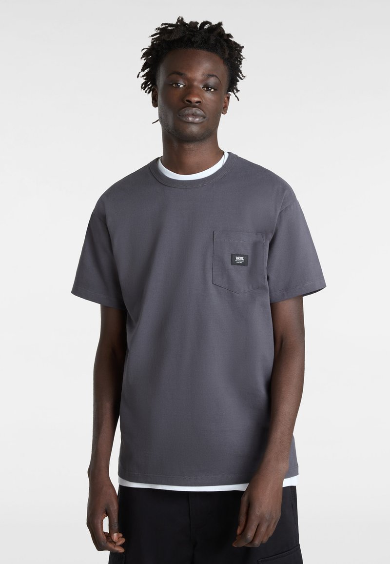 Camiseta de algodón gris con cuello redondo, mangas cortas y un bolsillo en el pecho. Presenta un interior del cuello en blanco a contraste y un parche con el logo.