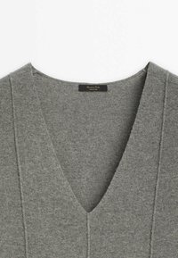Pull gris en tricot à col en V avec des détails de coutures visibles et une étiquette noire à l'arrière du col.