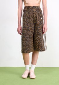 Bruna leopardmönstrade culotter med vita sidosträck och lös passform. Bärs med ljusrosa sneakers och vita strumpor.