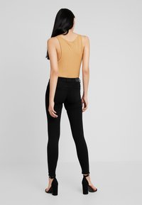 Top de tirantes ajustado de canalé en mostaza, combinado con jeans skinny negros y sandalias de tacón con tiras en el tobillo. Diseño simple y elegante.