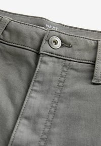 Graue Baumwollhose mit einem Frontknopfverschluss, sichtbaren Nähdetails und einer glatten Textur. Etiketten an der Taille enthalten.