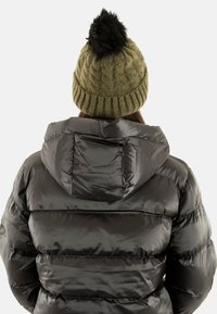 Chaqueta acolchada negra con capucha, fabricada con material brillante y un diseño acolchado. Combinada con un gorro de punto verde oliva texturizado rematado con un pompón negro.