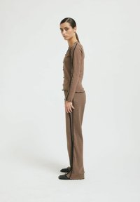 Braunes Strick-Loungewear-Set mit einem langärmeligen Oberteil mit Knöpfen und gewellten Kanten, kombiniert mit ausgestellten Hosen mit seitlichen Akzenten.