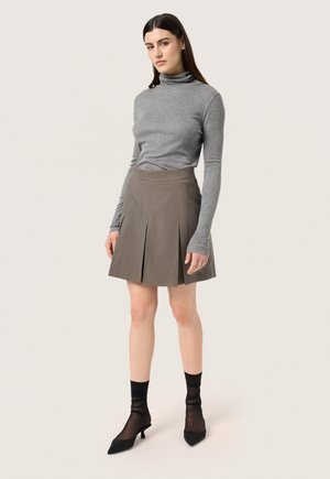 Šedý rolák spárovaný s plisovanou béžovou sukní. Černé průsvitné ponožky a lodičky se špičatou špicí dotvářejí outfit. Jednoduchý, moderní design.