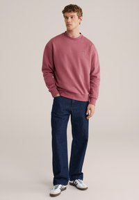 Temno rdeč pulover s krožnim izrezom, rebrastimi manšetami in spodnjim robom; kombiniran s temno modrimi jeans hlačami. Obleka vsebuje bele superge s črnimi poudarki.