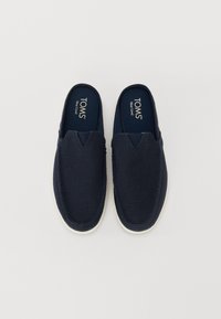 Marineblå slippersko med et teksturert stoffoverdel og hvit gummisåle. Har et utskåret design foran for enkel påkledning.