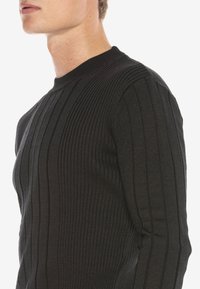 Schwarzer, gerippter Strickpullover mit langen Ärmeln, der vertikale Streifen und einen runden Halsausschnitt bietet. Hergestellt aus einem weichen, strukturierten Stoff.