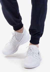 Scarpe da ginnastica bianche con upper in rete e sintetico, punta tonda, design con lacci e collo imbottito, indossate con pantaloni jogger blu navy.