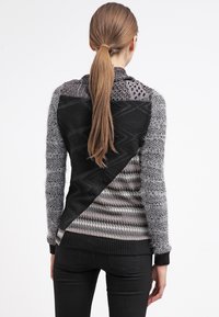 Pull noir et gris à motifs avec textures variées, présentant des designs géométriques, des poignets côtelés et une silhouette légèrement asymétrique.
