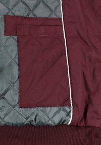 Burgundy quiltad jacka med en grå ficka, som har en vit accent söm och ribbad nederkant, som visar en slät textur.