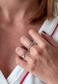Három ezüstgyűrű egy kézen. Az egyik csillagmotívumot, a másik csavart textúrát, a harmadik pedig leveles formát mutat, fényes felülettel.