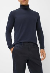 Marineblauw shirt met lange mouwen en col, gemaakt van zachte stof, met een getailleerd ontwerp en contrasterende donkere manchetten, gecombineerd met donkere broeken.