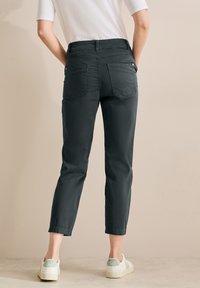 Tmavě �šedé kalhoty slim fit s manžetami na kotnících a zadními kapsami. Kombinované se světlejšími teniskami se zeleným akcentem.
