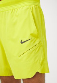 Neon žute sportske kratke hlače od laganog materijala, s bočnom džepom na zatvarač i crnim Nike logotom.