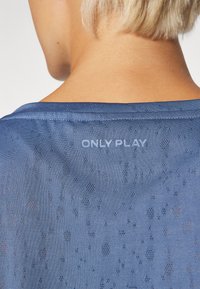Zils sietu apģērbs ar smalku rakstu, ar noapaļotu kakla izgriezumu un baltiem vārdiem "ONLY PLAY" aizmugurē.