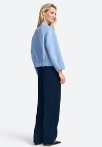 Giacca cropped azzurro chiaro con maniche larghe e vita elasticizzata, abbinata a pantaloni navy a gamba larga e scarpe nere a punta.
