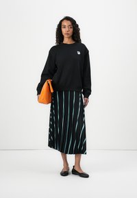 Black sweatshirt with a white flower emblem, paired with a pleated black skirt featuring teal stripes. Orange clutch bag and black flats.