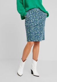 Falda lápiz de tela con estampado floral en azul y verde, con dos bolsillos frontales. Combinada con botas de tobillo blancas de estilo western.