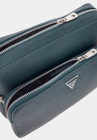 Portofel din piele verde-albastru, cu fermoar, având două compartimente, accesorii din argint și o căptușeală interioară cu model ce prezintă logo-ul brandului.