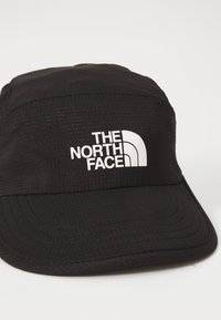 Casquette noire en tissu texturé avec un logo blanc "The North Face" et une visière incurvée. Design simple sans accents supplémentaires.