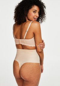 Sujeción nude de encaje en la espalda con tirantes ajustables y braga alta de tejido suave. Ambas piezas presentan tonos neutros y un diseño sin costuras.