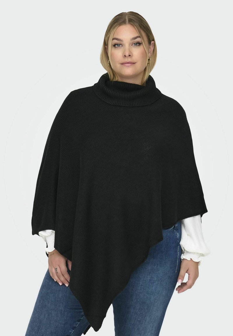 Poncho en tricot noir avec un col roulé haut et côtelé. Présente un ourlet fluide et asymétrique ainsi qu'un motif texturé. Porté par-dessus une chemise blanche.