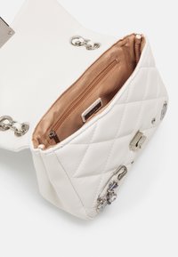 Borsa a tracolla bianca trapuntata con una catena argentata, dotata di un interno beige, tasca con zip e hardware decorativo con dettagli blu.