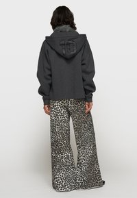 Haut à capuche gris court avec une finition texturée et un grand "10" dans le dos, associé à un pantalon large en imprimé léopard.