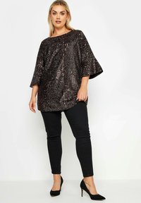 Top nero con paillettes, dal taglio ampio e maniche larghe, abbinato a pantaloni neri aderenti e tacchi alti neri. Texture liscia e lucida.