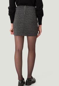 Jupe mini grise à motifs avec une fermeture éclair dissimulée à l'arrière. Le mannequin porte des collants opaques noirs et des mocassins noirs brillants.