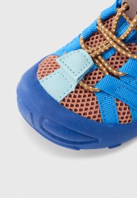 Αθλητικό παπούτσι με καφέ πλεκτό πάνω μέρος και μπλε συνθετικές λεπτομέρειες, αντιολισθητική μπλε σόλα και κορδόνια σε χρυσοκαφέ για ασφαλές δέσιμο.