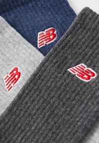 Three pairs of ribbed socks in grey, navy, and dark grey. Each features a red embroidered logo. Texture appears soft and stretchy.
