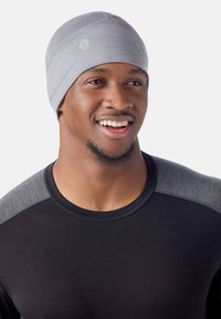 Beanie grigio chiaro in un design aderente, realizzato in un materiale liscio e elasticizzato. Presenta dettagli di cucitura sottili e un emblema con logo.