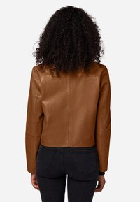 Bruine leren jas met een cropped ontwerp, met lange mouwen en een gladde textuur. Gecombineerd met donkere jeans, met een eenvoudige achterkantweergave.