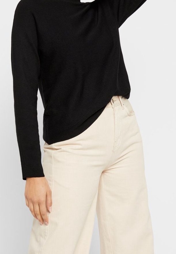 Pull en maille noir à manches longues, associé à un pantalon beige à jambe large, avec une coupe décontractée et une texture subtile. Aucun motif ou détail visible.