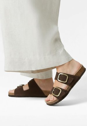 Brune ruskindssandaler med to brede remme og metalspænder, med en korkfodseng og tekstureret gummisål.