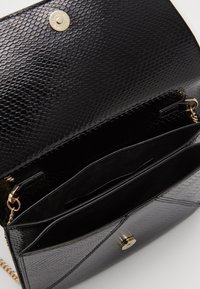 Sac à main en simili cuir noir avec une finition texturée, quincaillerie dorée, fermeture magnétique et plusieurs compartiments intérieurs.