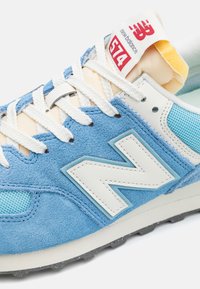 Blå mocka och nät sneaker med vita läderdetaljer, framträdande 'N' logotyp och krämfärgade snören. Har en vadderad tunga och texturerad sula.