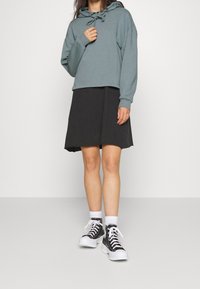 Sudadera azul claro con cordones y mangas largas, combinada con una falda negra hasta la rodilla y zapatillas altas en blanco y negro.