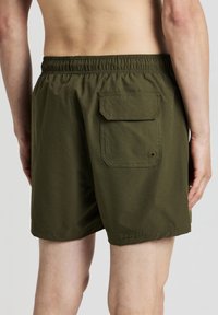 Olivgrüne Schwimmshorts mit strukturierter Oberfläche, elastischem Bund und einer aufgesetzten Gesäßtasche mit Knopfverschluss.