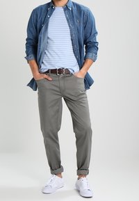 Camisa de mezclilla, camiseta de rayas azul clara, pantalones grises y zapatillas blancas. Ajuste casual con puños enrollados y cinturón marrón.