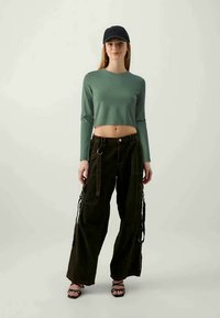 Πράσινο μακρύ μανίκι cropped top συνδυασμένο με σκούρους πράσινους φαρδιούς cargo παντελόνες με πλάγιες τσέπες και αντίθετους ιμάντες. Μαύρο καπέλο και σανδάλια.