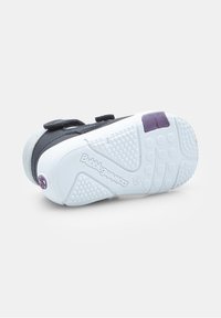 Sneaker nera e grigia con suola in gomma. Presenta strap in velcro, un accento viola sul tallone e una suola testurizzata per una buona aderenza.